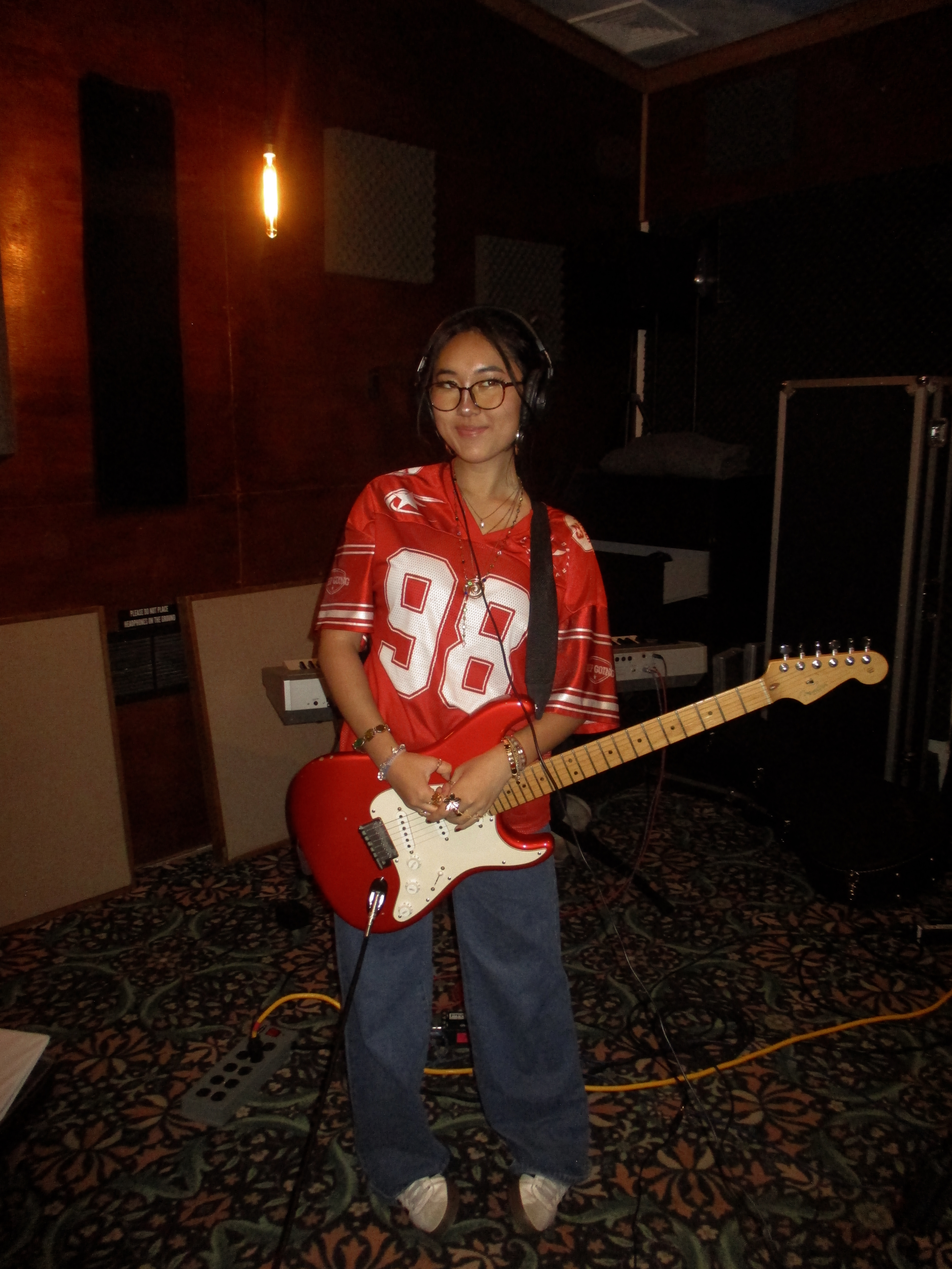 Shuhan Li in the studio, wearing a red jersey with a red guitar